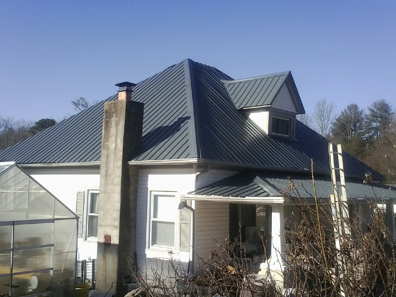 Dark blue standing seam metal roof on a white farmhouse with dormer — Slate & Tile Roof Repair by Roofing Brothers in Means