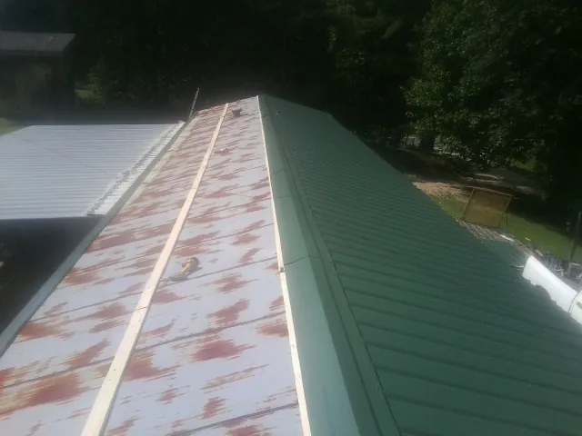 Old rusted panels beside newly installed green metal roofing — Wind Damage Roof Repair by Roofing Brothers in Means