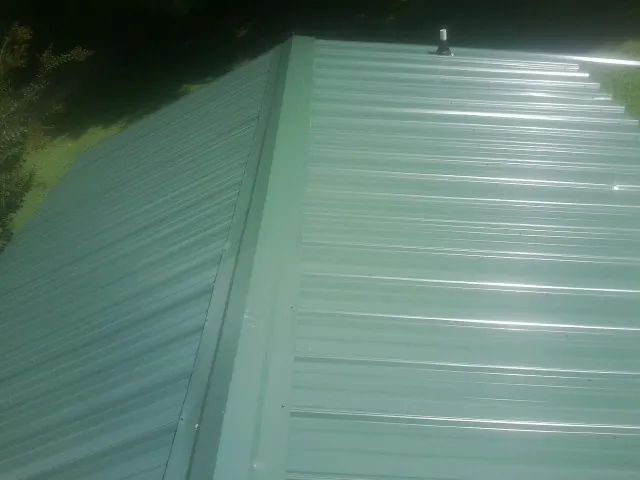 New green metal panels meeting at the ridge of a roof — Flat Roof Repair work by our crew in Means