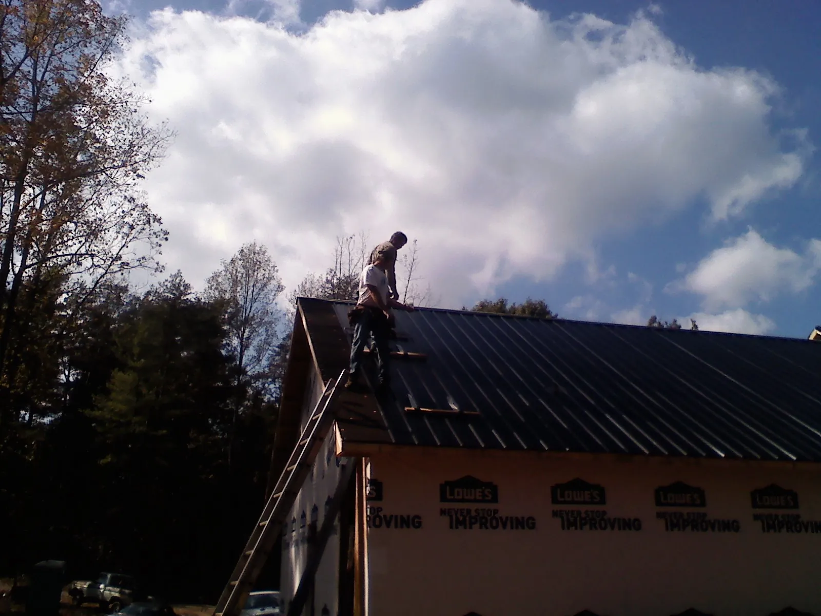 Roofer fastening dark metal panels high against a cloudy sky, from a Roof Inspection job in Means