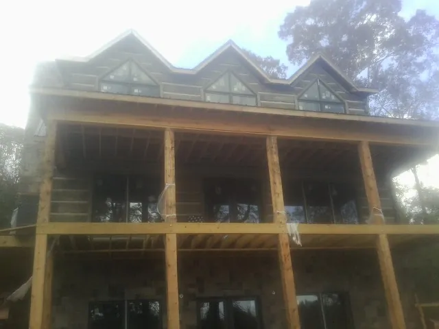 Dormers and porch framing on a large log home under construction — Roof Coating work by our crew in Means