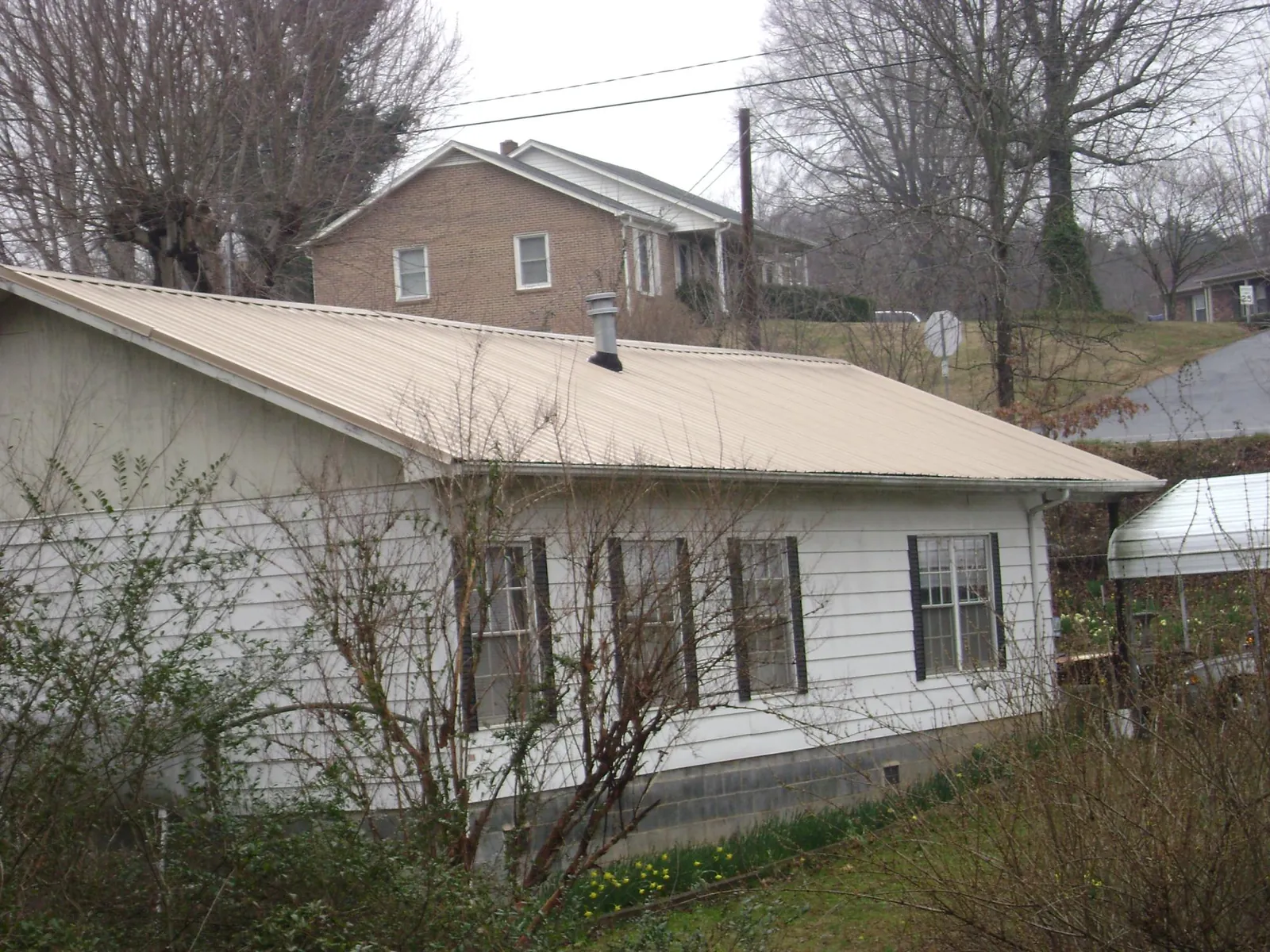 Tan metal roof on a white sided house set into a hillside — Commercial Roofing by Roofing Brothers in Means