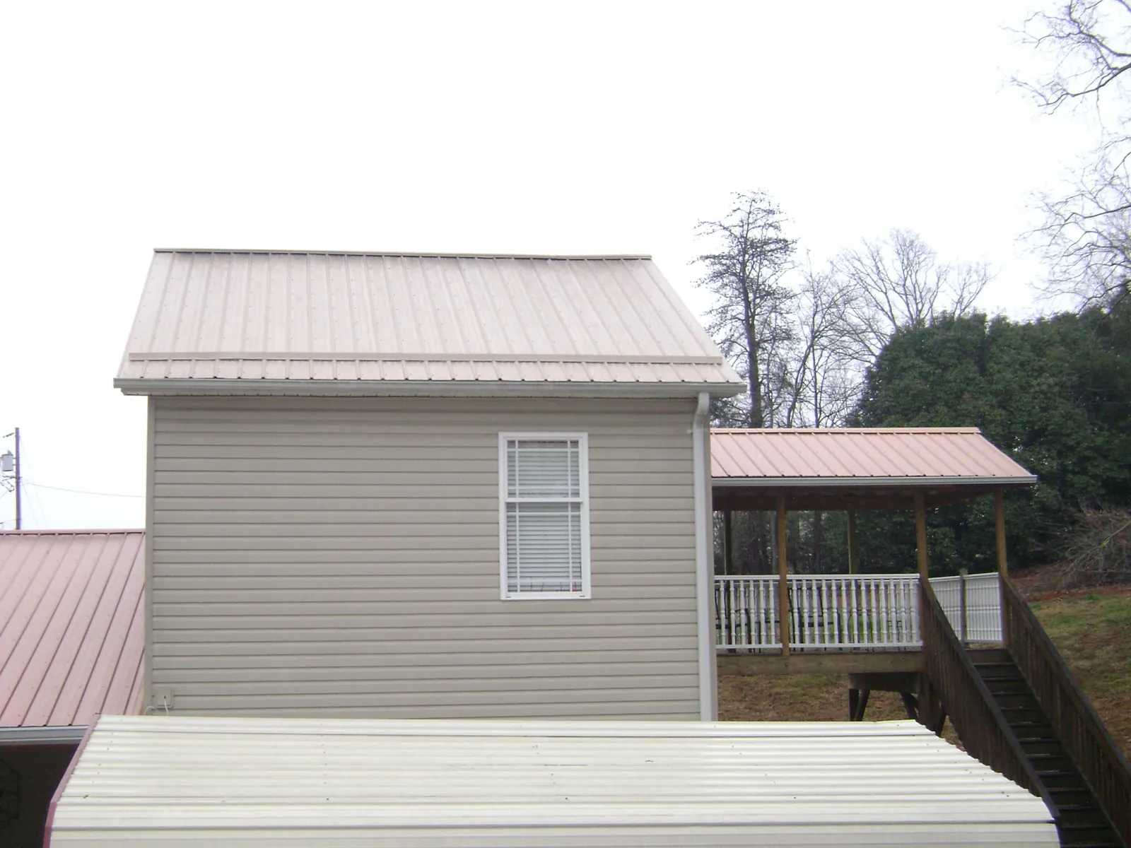 Tan metal roofs on a two story addition and attached porch, from a Roof Replacement job in Means