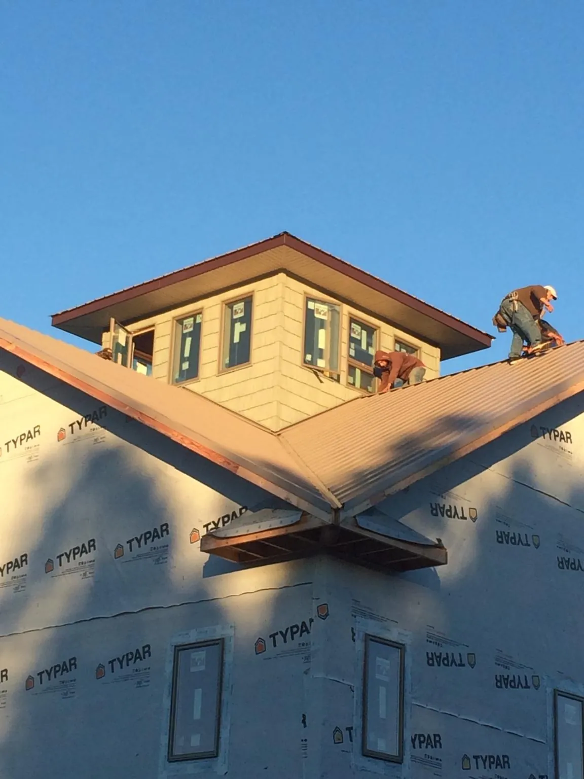 Roofers working around a rooftop cupola on a new metal roof at sunset — Roof Waterproofing in Means by Roofing Brothers